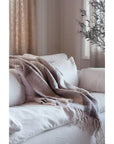 A cream sofa features the Indaba Checkerboard Throw in Taupe, its modern beige and brown pattern draped stylishly, set in a softly lit room with light walls and a leafy plant in the background.