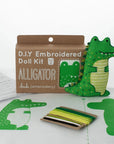 The Faire Alligator Embroidery Kit includes green and white thread, pre-cut fabric with an alligator pattern, stuffing, instructions, and a finished sample—everything needed to craft your own alligator plush.