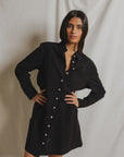A woman poses in front of a light backdrop, wearing the long-sleeved Felicia Poplin Dress by Perfectwhitetee—a black cotton poplin shirt dress with white buttons—ideal for everyday wear.