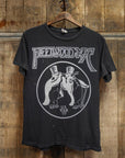 The Made Worn Fleetwood Mac Tee is a vintage unisex black t-shirt with two penguins in top hats and "U.S. Tour '77" under the band's logo, made in the USA and displayed on a wooden hanger against a rustic wood wall.