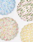 The Faire Mixed Set Reusable Large Plates features four scallop plates with floral patterns—blue, pink, yellow, and multicolor—on light backgrounds. Perfect decorative party plates for any cheerful gathering.
