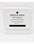 A white box labeled "Fritz & Troy Fresh & Breezy Candle," hand-poured in NYC. This coconut/soy wax candle offers an ocean breeze scent and naturally eliminates odors. Net wt: 7 oz.