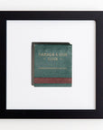 A framed matchbook with a green and brown design is centered against a white background. The matchbook displays the text "GARDEN & GUN CLUB" and "GARDENANDGUNCLUB.COM" in gold lettering. The black frame contrasts elegantly with the design, making it a refined piece for prints enthusiasts. This piece is called the Art Square Blk Frame by Match South.