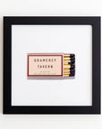 An Art Square Blk Frame from Match South, located at 42 East 20th Street, New York, NY 10003, displayed on a white background. The matchbox has a brown and beige design with yellow matches partially visible. Encased in clear acrylic, the black frame enhances its vintage charm.