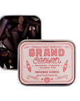 An open tin of G&W Incense by Faire with a pink and red design reveals dark brown cones. The label notes cedarwood, labdanum, and charred pine scents for an earthy incense experience.