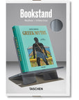 A turquoise "Greek Myths" book sits on an Ingram Book Company Bookstand Md in urban grey, featuring a male figure with a sword on the cover and packaging labeled "Bookstand Medium — Urban Grey.