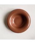 The Faire Gyrus Pocket Tray—a round, smooth, brown ceramic bowl with a wide rim—rests on white fabric atop a concrete tray, seen from above.