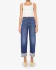 A woman wears a white sleeveless top and Mother’s Half Pipe Ankle high-waisted barrel jeans with a cuffed frayed hem, paired with pointed yellow shoes, standing against a plain white background.