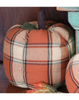 The Faire Pumpkin features a cozy orange, cream, and brown plaid fabric with a brown stem and green fabric leaf, making it ideal farmhouse decor or a charming fall ornament for your home.