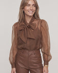 LS French Bow Shirt with puffed sleeves by THE SHIRT, styled with brown leather pants, neutral backdrop.