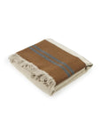 The Highland Coverlet by Libeco Home is a folded, rectangular coverlet with beige fringe edges, featuring a brown and beige color block design and two parallel dark gray Highland Stripe accents from the linen/wool collection.
