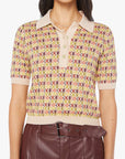 A woman wears The Hot Under the Collar Polo by Mother—a cropped, patterned knit top with a beige collar and buttons—paired with high-waisted maroon belted pants. Her face is not visible.