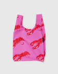The Baby Baggu by Baggu is a pink reusable shopping bag made from recycled ripstop nylon, featuring red lobster prints. It is shown against a simple light background.