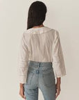 A person with long dark hair wears the Huguette Top by DOEN with lace sleeves and high-waisted blue jeans, standing with their back to the camera against a plain background.
