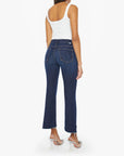 A woman stands facing away, wearing Mother’s The Insider Crop Step Fray high-waisted bootcut jeans in stretch denim with frayed hems and a white sleeveless top, paired with clear heels, against a plain white background.