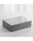 The 9.94039 Interwoven Box LG by Global Views, featuring a geometric black-and-white star pattern, sits on a light surface before sheer white curtains.