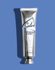A metallic tube labeled "Jao Hand Salve, Jao Limited, 1 oz/28g" stands upright on a blue background with a left-cast shadow—ideal for moisturizing dry hands and feet with nourishing shea oil.