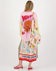 A woman faces away, showcasing a colorful, eclectic ensemble featuring patterns and text like "WINNER" and a cartoon octopus on her matching shirt. She wears the Vanessa Midi Skirt by Me369 with an elastic waist, carries a patterned bag, and completes her look with red sandals.