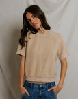 A woman with long brown hair wears the Perfectwhitetee Kennedy SS Crew Sweatshirt in beige and blue jeans, standing with her hands in her pockets against a neutral fabric backdrop.