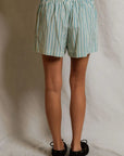 A person stands facing away from the camera, wearing Perfectwhitetee’s Julie Poplin Short—light blue and white vertical stripes—paired with black ballet flats, set against a plain white backdrop.