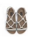 The Roam Linky Sandal features tan contoured footbeds and metallic silver vegan leather crisscross straps, with "ROAM" labels on the insoles. Shown from above on a white background.