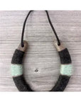 The Faire Lucky Horseshoe is a handmade necklace with a U-shaped pendant, crafted from upcycled horseshoes and wrapped in dark gray and mint green thread—an eco-friendly housewarming gift on a thin black cord.