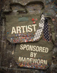 The limited-edition Artist Tote by Made Worn is crafted from cotton canvas with paint splatters, polka dot ribbons, confetti accents, and playful pins—one says "ARTIST," the other "SPONSORED BY MADEWORN." Each bag is truly unique.