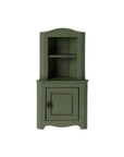 The Maileg Corner Cabinet by Maileg is a compact green wooden unit with an upper shelf and a closed door below, providing space-saving storage. It is shown against a plain white background.