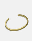 The Curated Basics MENS Flat Cuff is a minimalist gold brass bracelet with a 5mm width and smooth matte finish, open-ended to elegantly wrap the wrist. Shown on a plain white background.