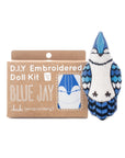 The Faire Blue Jay Embroidery Kit comes in a brown package with a blue jay design. Next to it, a finished plush blue jay doll is sewn in blue, white, and black.