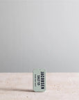 A small rectangular tin labeled "Faire Kosher Sea Salt slide Tin" stands upright on a light textured surface, offering convenient, travel-sized kosher sea salt against a plain, light gray background.