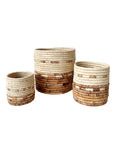 The Amsha - Faire Mkongo Plant Baskets, in three sizes, feature a natural to brown gradient pattern and are displayed side by side on a white background.