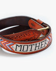 The Eye Opener by Mother is a vintage brown cow leather belt featuring "MOTHER" spelled in white, black, and gray beads, with vibrant blue, orange, and red geometric patterns along the edges.