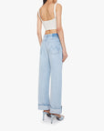 A woman shown from the back wears Mother’s The Dodger Button Hover Cuff: loose, light blue straight-leg jeans with turned-up cuffs, paired with a beige cropped tank top and light blue high-heeled sandals.