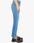 A person standing sideways wears the Mother Lil Insider Crop Step Fray high-waisted bootcut light blue jeans with frayed hems and black tassel loafers, set against a plain white background.