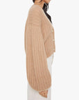 A woman in Mother’s The Puffy Sleeve Varsity Cardi, an alpaca blend chunky knit beige cropped cardigan with large buttons, paired with high-waisted white pants, shown in side profile against a white background.
