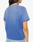 A woman with long dark hair is seen from the back, wearing Mother’s The Short Sleeve Concert Tee and light blue jeans against a plain white background.