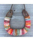 The Faire Lucky Horseshoe features a rustic upcycled horseshoe wrapped in colorful yarn and suspended by a leather cord, making it a unique housewarming gift.