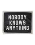 The Oxford Pennant Nobody Knows Anything Camp Flag is a black and white rectangular flag with a white border, corner grommets, and bold text reading "NOBODY KNOWS ANYTHING," perfect for embracing a clueless spirit.