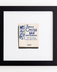 A framed vintage matchbook cover with blue text and illustrations from "Famous Oyster Bar Restaurant" located at 842 7th Avenue, Corner 54th St., N.Y.C. The matchbook is centered in a white mat with a sleek black frame, now enhanced by clear acrylic to protect its vibrant prints. This is the Art Square Blk Frame by Match South.