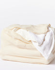 The Coyuchi Inc Organic Laundry Bag XL in beige, made from organic cotton mesh, sits against a white background, filled with white towels. One towel is partially draped over the edge of this natural laundry solution.