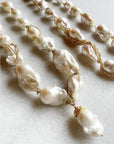 Close-up of Bittersweet Designs' Short Wrapped Pearls w/ Pearl Drop: irregular baroque pearls entwined with delicate gold chains on marble, featuring a front pearl with a decorative gold cap for an elegant, artistic finish.