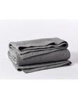 A Coyuchi Inc Pebbled Org Quilt Queen in Slate is folded and stacked on a white surface.