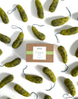 A box labeled "Pickle" is surrounded by several green Faire Felted Ornaments shaped like pickles, each with a loop for hanging, all displayed on a white background.