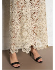Close-up of a person wearing black open-toe heels and the SUNCOO Fanny Skirt, featuring intricate crochet floral lace, set against a white wall and brown floor.