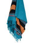 The Sackcloth & Ashes/ Yellowstone Teal by Sackcloth & Ashes is a turquoise and black scarf with orange, yellow, and blue stripes, fringe ends, and a fabric label. Inspired by the Yellowstone blanket and made from recycled materials.