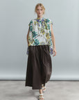 A person wears Psophia's 2684 Womens Trouser with a sleeveless, floral cotton poplin blouse featuring a ruffle neckline and white sandals, standing against a light gray background.