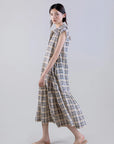 A woman stands sideways in a Psophia Soft-Touch Plaid A-Line Drop-Waist Dress, sleeveless and ankle-length, styled with beige slip-on shoes against a plain light gray background.