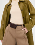 A woman in an olive green leather coat, beige turtleneck, and tan wide-leg pants stands with one hand in her pocket, accessorized with the Rachel Comey Double Wrap Hamcon Belt with Pouch featuring gold-tone hardware.