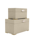 Two Ramato Boxes by The Import Collection—beige fabric storage boxes with gold-tone handles and feet—stacked together against a white background, ideal for adding stylish, modern decor to your home.